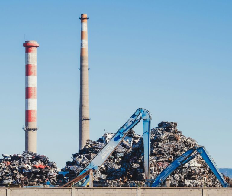 Industrial scrapyard with smokestacks and cranes on a clear day.